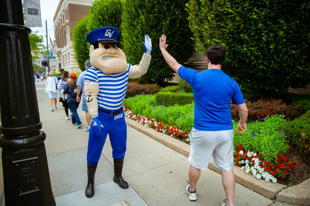 Louie the laker high five-ing a student as they walk on the sidewalk